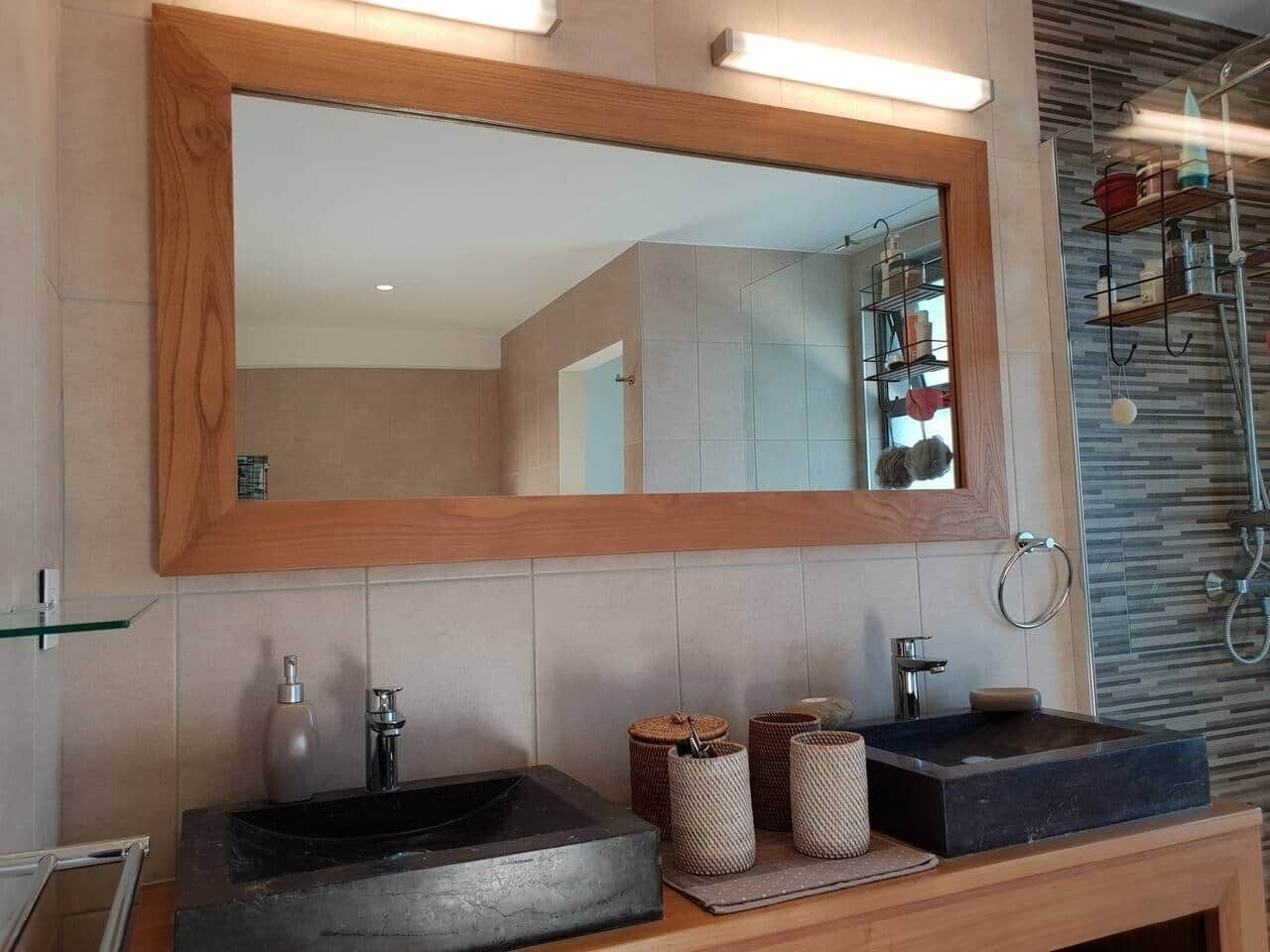A modern bathroom with a large mirror, two sinks, and a shower area.