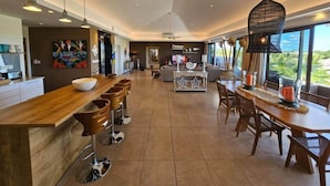 A spacious kitchen with a long counter, bar stools, and a dining area with a table and chairs. - Penthouse avec Jacuzzi Privé à Pereybère (Grand Baie)