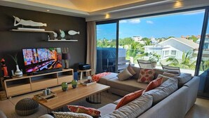 A modern living room with a large sofa, a coffee table, and a TV on a wooden stand. - Penthouse avec Jacuzzi Privé à Pereybère (Grand Baie)