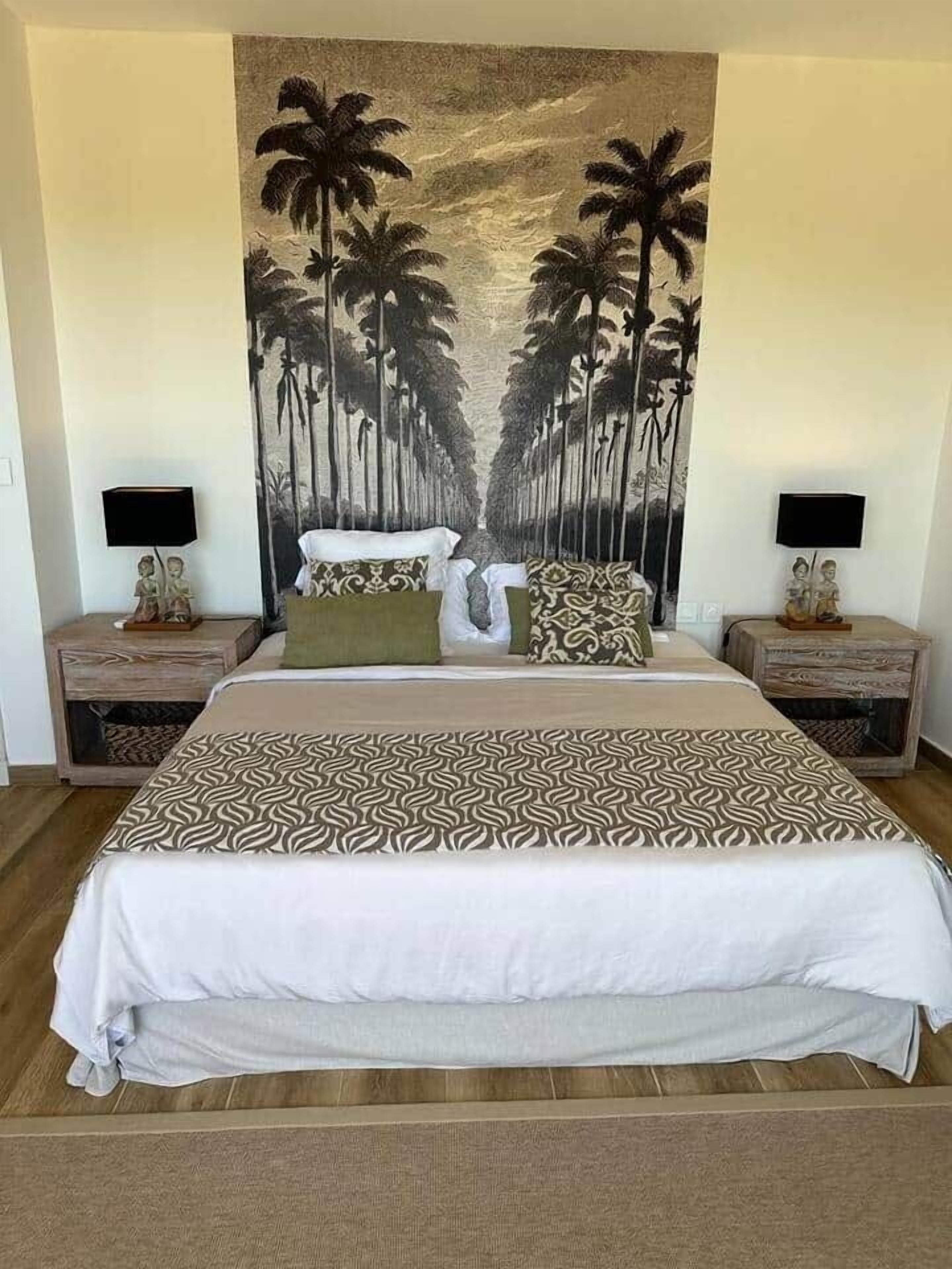 Un dormitorio con una cama grande, dos mesitas de noche, un mural en la pared y un televisor montado en la pared.