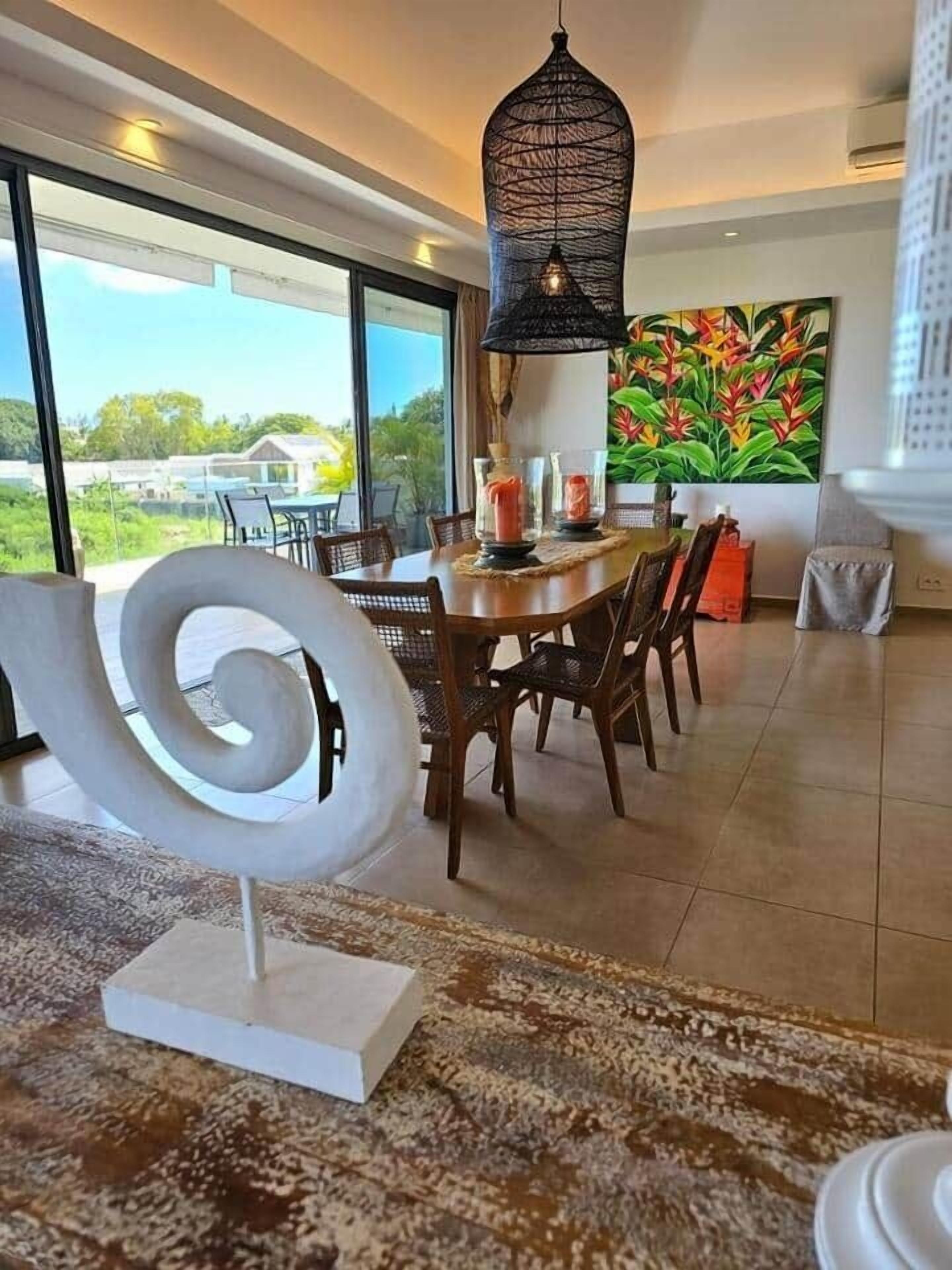 Un espace repas comprenant une grande table, des chaises, une sculpture en spirale décorative et une vue sur la verdure environnante.