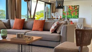 A modern living room with a grey sofa, orange cushions, a wooden coffee table, and a wicker chair. - Penthouse avec Jacuzzi Privé à Pereybère (Grand Baie)