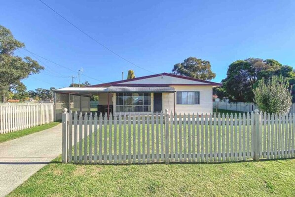 A single-story house with a fenced yard, a covered porch, and a clear sky.