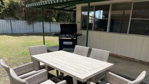 A patio with a table and wicker chairs, a grill, and a covered area. - Comfortable 2-Bedroom home “Rest Easy Mudgee” (Mudgee)