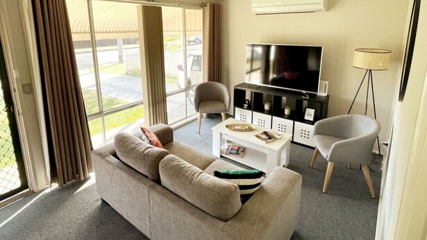 A modern living room with a sofa, a coffee table, a TV, and a lamp. - Comfortable 2-Bedroom home “Rest Easy Mudgee” (Mudgee)