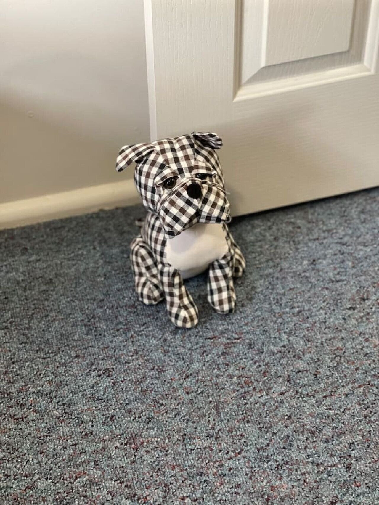 Eine kleine, karierte Hunde-Figur auf einem gemusterten Teppich neben einer weißen Tür.