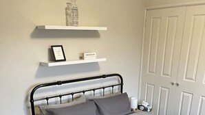 A bedroom with a bed, a bedside table, a lamp, a shelf with items, and a door. - Comfortable 2-Bedroom home “Rest Easy Mudgee” (Mudgee)