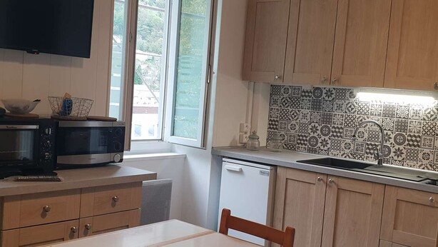 A compact kitchen with wooden cabinets, a microwave, a sink, and a window providing natural light. - Renovated central studio, 50 m from cable car, 2-4 pers (Cauterets)