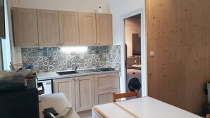 A compact kitchen with wooden cabinets, a tiled backsplash, and a washing machine in the adjacent room. - Renovated central studio, 50 m from cable car, 2-4 pers (Cauterets)