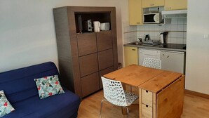 A compact living space with a sofa, a wooden table, a white chair, a kitchenette, and a cabinet.