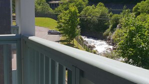A balcony with a view of a river, a car on the road, and a building in the background.