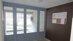 A room with a large glass door, a bulletin board with notices, and a black doormat.
