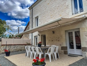 Un bâtiment en pierre doté d’un patio couvert, de sièges en plein air et d’un pot de fleurs orné de fleurs rouges.