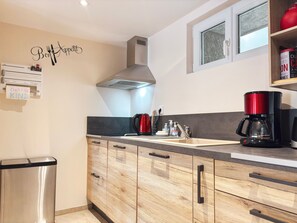 Una cocina moderna con armarios de madera, un cubo de basura de acero inoxidable, una cafetera roja y un letrero en la pared.