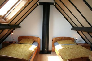A room with two wooden beds, a central black chimney, and skylights.
