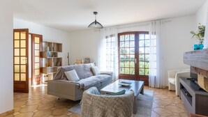 A living room with a sofa, coffee table, and TV stand. There is a bookshelf and a door leading to a balcony.