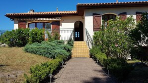 A house with a paved entrance, a tiled roof, and a garden with various plants.