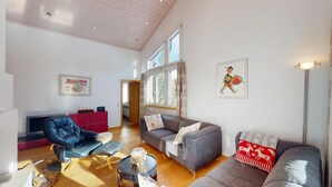 Amplia sala de estar con diseño moderno, que incluye un sofá gris, un mueble de entretenimiento rojo y un gran ventanal que proporciona luz natural.