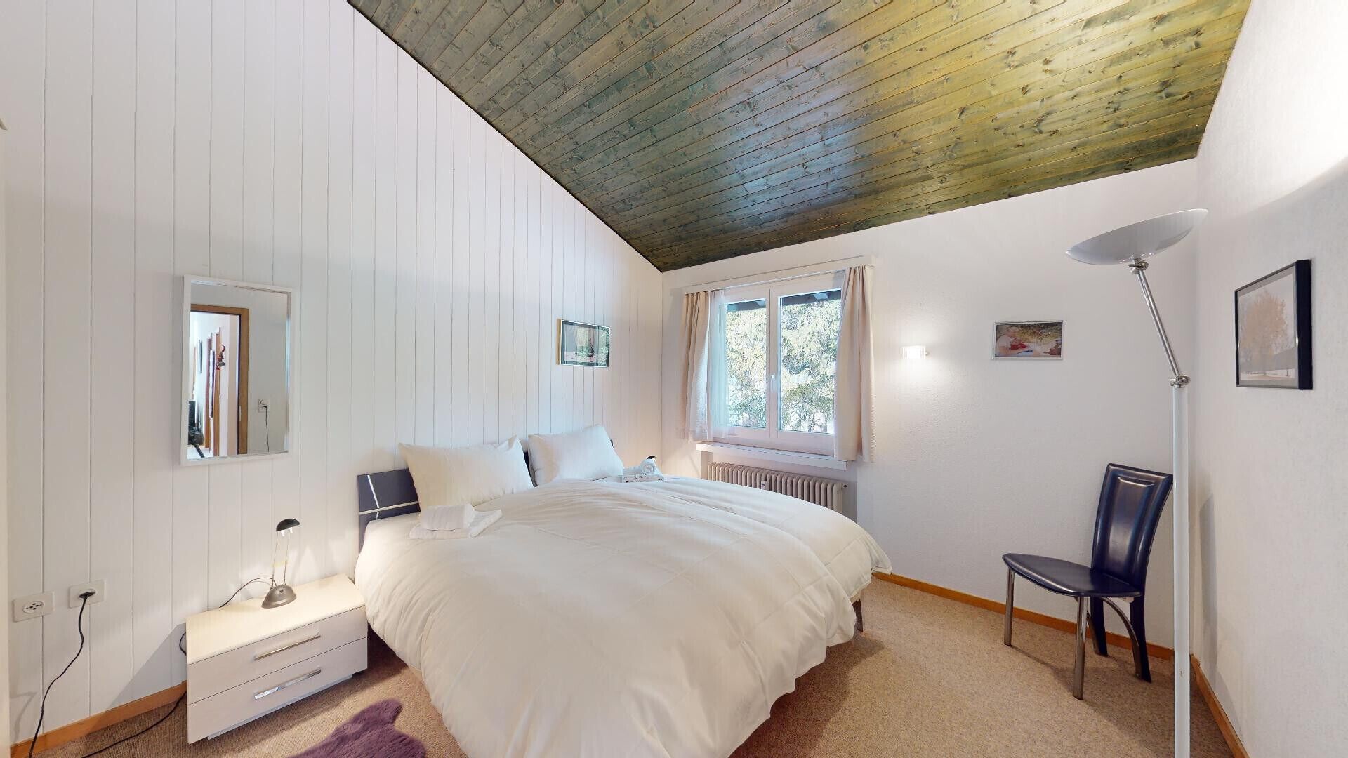 Une chambre à coucher comprenant un lit, une table de chevet, une chaise, une fenêtre et un radiateur.