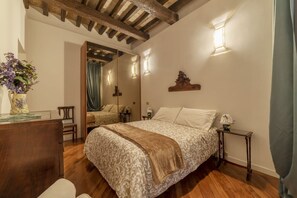 A bedroom with a wooden ceiling, a bed with patterned bedding, a nightstand, a mirror, and a vase with flowers.