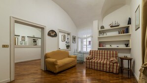 Un saló amb terra de fusta, un sofà beix, un butacó rayat i una biblioteca amb objectes decoratius.