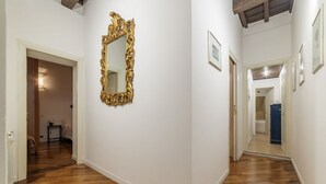 Un passadís amb paviment de fusta, un mirall gran i ornamentat, i quadres amb marc a les parets.