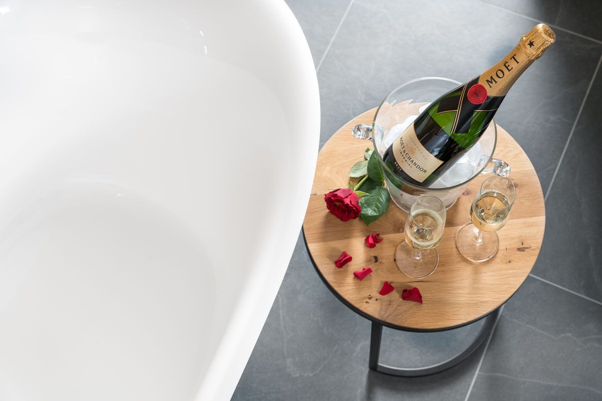 Une bouteille de champagne Moët, deux verres et une rose sur une table en bois dans une salle de bain.