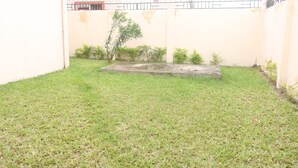 A grassy courtyard with a concrete structure, a wall with barbed wire, and a building with a red roof in the background.
