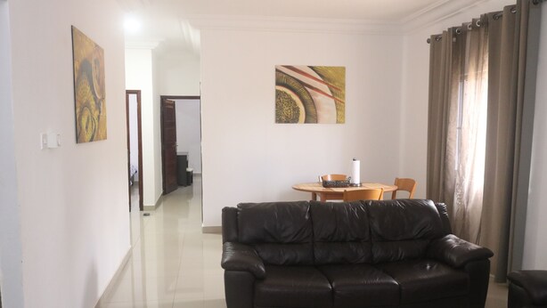 A living room with a black leather sofa, a wooden dining table with chairs, and two abstract paintings on the walls.