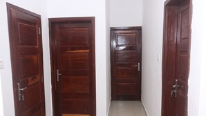 A hallway with three wooden doors, each with a metal handle and a keyhole. The floor is tiled, and the walls are white.