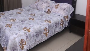 A neatly made bed with a patterned bedspread, a dark headboard, and a nightstand with a drawer.