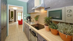 Een moderne keuken met een ingebouwde magnetron, een gasfornuis en een spoelbak. Op het aanrecht staan potplanten en er staat een rode stoel op de achtergrond.