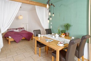 A cozy room with a bed, a dining table with chairs, a hanging light fixture, and a potted plant.