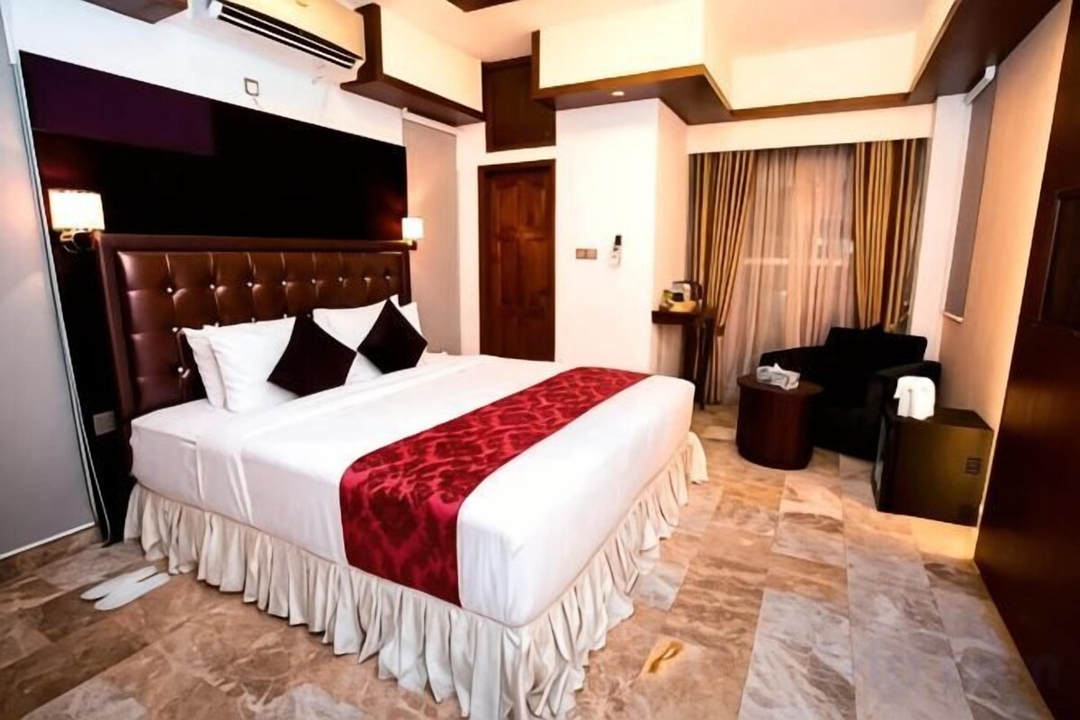 Ein Hotelzimmer mit einem großen Bett, einem Holzkopfstück, einer roten Zudecke und einem Marmorboden.