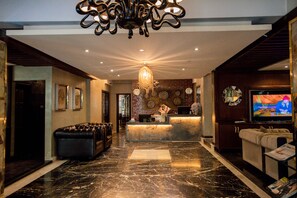 A lobby with a reception desk, a leather sofa, a chandelier, and a television. - The Elite Residence Dhaka. (Dhaka)