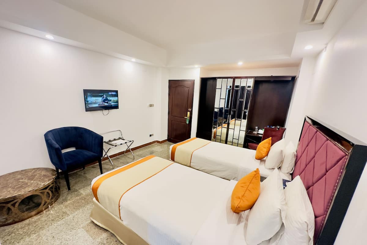A hotel room with two beds, a TV, a chair, and a small table.