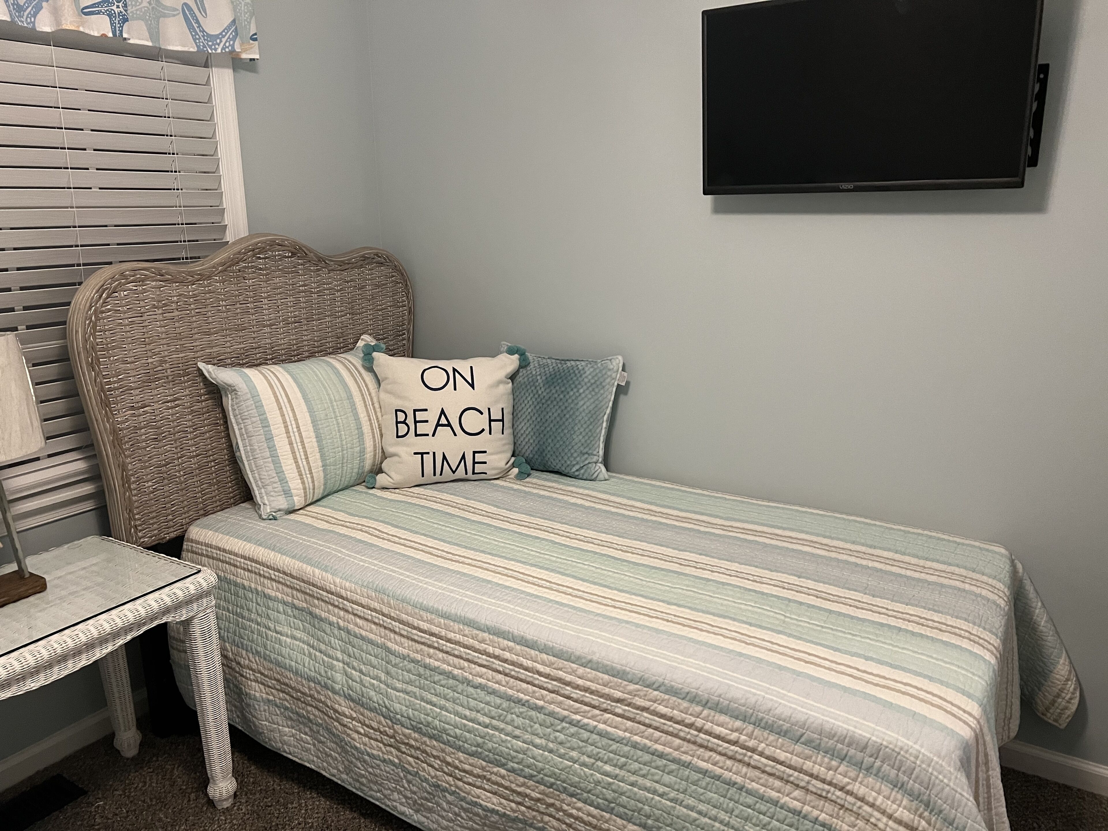 A bedroom with a bed, pillows, a television, a wicker chair, and a table.