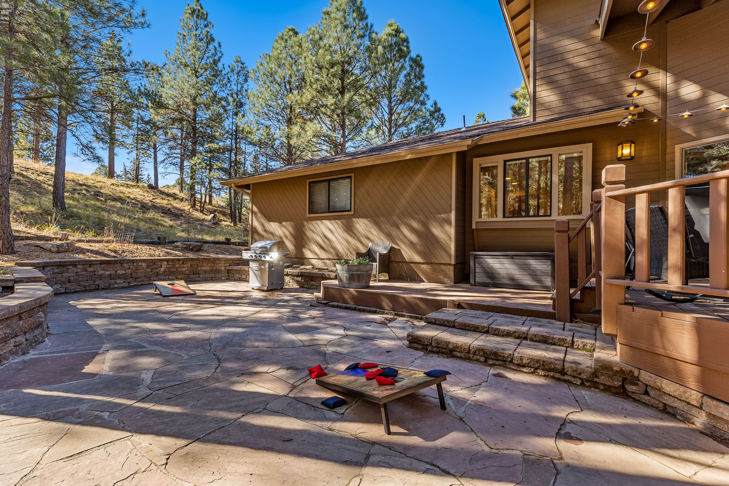 A patio area with a stone floor, a wooden table with cushions, and a barbecue grill.
