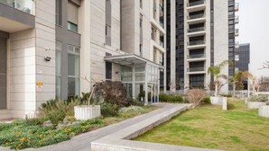 A modern building with multiple floors, large windows, and a landscaped garden area with pathways and plants. - Luxury 3BR 32 Floor SeaView (Bat Yam)