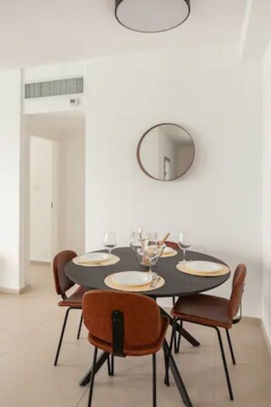 A dining area with a round table, four chairs, and a wall-mounted mirror.