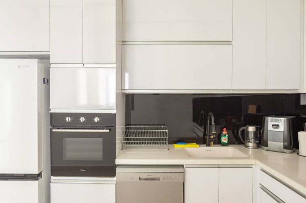 A modern kitchen with white cabinetry, a built-in oven, a dishwasher, and a coffee maker on the countertop.
