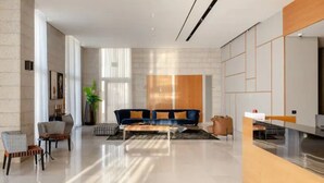 A modern hotel lobby with a sofa, chairs, a reception desk, and a large window. - Luxury 3BR 32 Floor SeaView (Bat Yam)