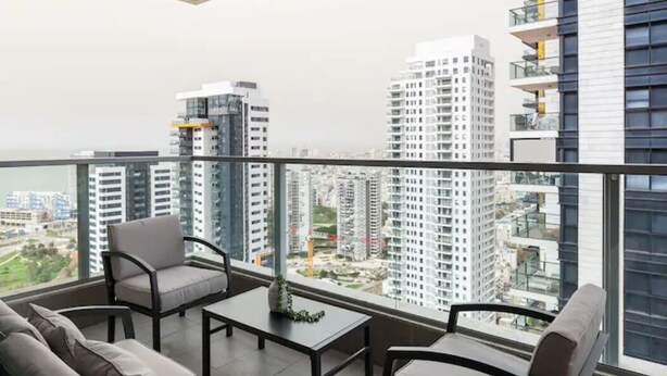 A balcony with a view of high-rise buildings, a sofa, and a table. - Luxury 3BR 32 Floor SeaView (Bat Yam)