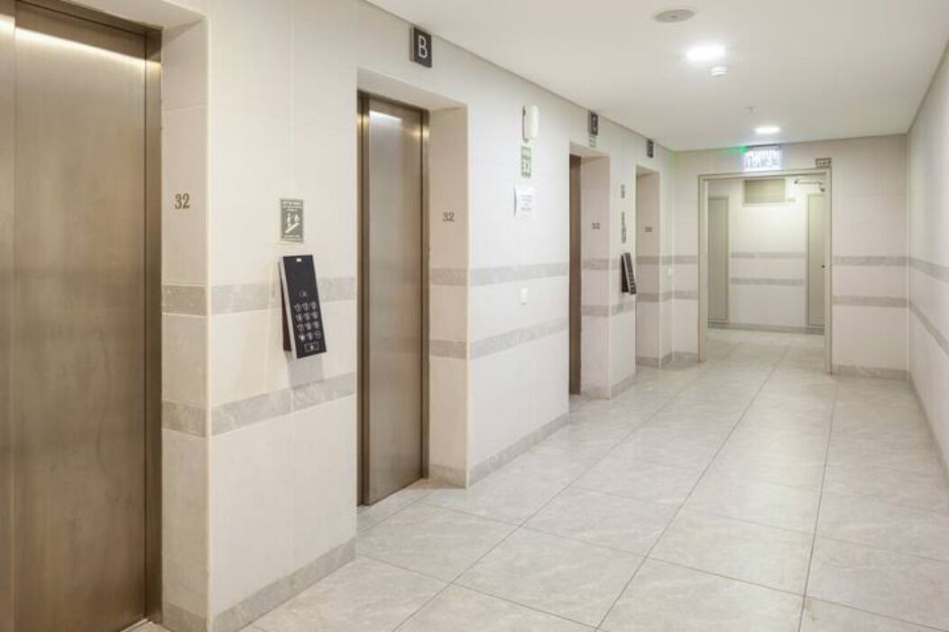 A hotel corridor with elevators, numbered doors, and a sign indicating the direction to the bathroom.