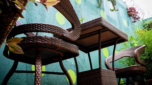 Wicker meubilair met een geweven ontwerp, geplaatst tegen een muur met groene planten en een schilderij.
