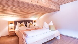 A wooden ceiling, a bed with pillows, and bedside lamps. - Apartment Pölvenblick - House Rabl (Itter)