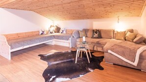 A cozy loft-style room with a wooden ceiling, a sectional sofa, a glass coffee table, and a black and white cowhide rug. - Apartment Pölvenblick - House Rabl (Itter)