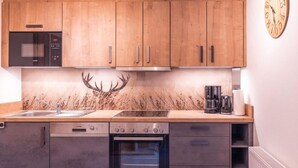 A modern kitchen with wooden cabinets, a microwave, a stove, an oven, and a clock on the wall. - Apartment Pölvenblick - House Rabl (Itter)