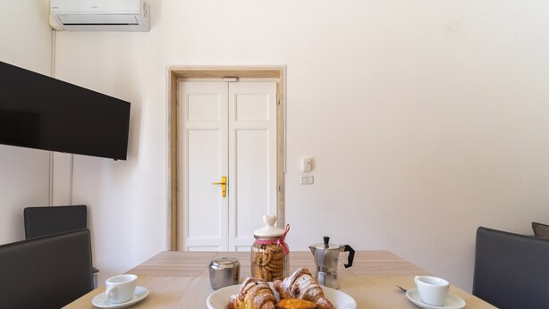 A dining table with a plate of pastries, a coffee pot, and a jar of cookies.