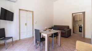 A compact living space with a dining table, two chairs, a sofa, a TV, and a kitchen area.